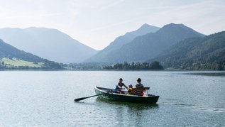 Eltern paddeln mit ihrem Kind in einem Paddelboot über den schönen Schliersee in Oberbayern.