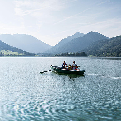 Eltern paddeln mit ihrem Kind in einem Paddelboot über den schönen Schliersee in Oberbayern.