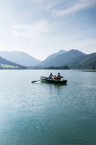 Eltern paddeln mit ihrem Kind in einem Paddelboot über den schönen Schliersee in Oberbayern.