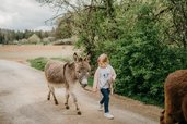 Ein Mädchen führt einen Esel entlang eines Waldwegs rund ums Familienhotel Friedrichshof.