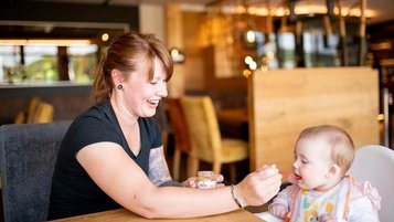 Mutter füttert ihr Baby liebevoll mit Brei im Familienhotel Landhaus zur Ohe.