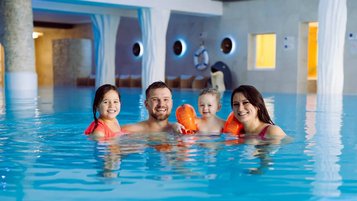 Familie badet gemeinsam im großen Hallenbad des Familienhotels Feldberger Hof und genießt unbeschwerte Momente im warmen Wasser.