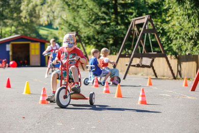 Kinder fahren im Außenbereich des Familienhotels Mein Krug im Fichtelgebirge mit Fahrzeugen durch einen Parcours aus Pylonen.