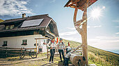 Zwei Mütter mit kleinen Kindern machen an einer Hütte eine Pause vom Wandern.