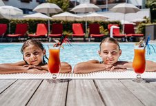 Zwei Mädchen genießen bunte Kinder-Cocktails am Poolrand des Familienhotels Amiamo an einem sonnigen Sommertag.