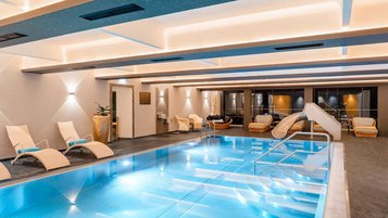 Heller Innenpool mit Treppe, kleiner Rutsche, bequemen Liegestühlen und stimmungsvoller Beleuchtung im Familienhotel Amiamo.