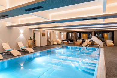 Heller Innenpool mit Treppe, kleiner Rutsche, bequemen Liegestühlen und stimmungsvoller Beleuchtung im Familienhotel Amiamo.