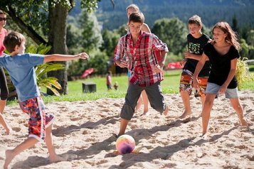 Teens spielen im Sand mit dem Ball auf dem Außengelände des Familienhotel Ramsi in Kärnten