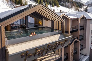 Außenansicht des Infinity-Pools des Hotels Zauchenseehof, in dem zwei Personen im warmen Wasser entspannen; der Pool ist in eine moderne Dachkonstruktion integriert und bietet einen Panoramablick auf die verschneiten Berge und Skipisten.