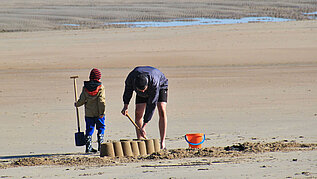 Vater und Sohn bauen am Nordseestrand mit Schaufeln und Eimern eine Sandburg.
