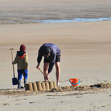 Vater und Sohn bauen am Nordseestrand mit Schaufeln und Eimern eine Sandburg.