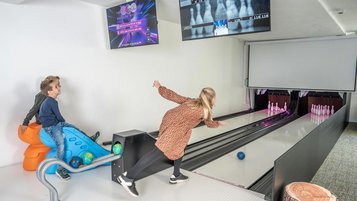 Eine Familie spielt auf der Mini-Bowlingbahn in der Teenslounge im Almfamilyhotel Scherer in Tirol