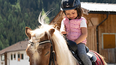 Mädchen sitzt im Reitunterricht im Familienurlaub im Alpenhotel Kindl auf dem Pferd.