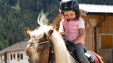 Mädchen sitzt im Reitunterricht im Familienurlaub im Alpenhotel Kindl auf dem Pferd.
