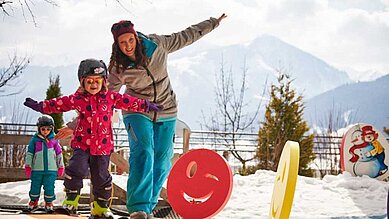 Skilehrerin bringt zwei kleinen Mädchen auf dem Zauberteppich des Familienhotels Amiamo das Skifahren bei.