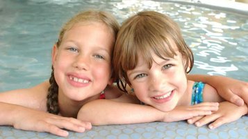 Zwei Kinder im Innen-Pool vom Familienhotel Am Rennsteig stützen sich am Rand ab und lächeln