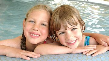 Zwei Kinder im Innen-Pool vom Familienhotel Am Rennsteig stützen sich am Rand ab und lächeln