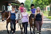 Jugendliche Mädchen führen Pferde auf denen Kinder sitzen über das Außengelände des Landhuus Laurenz.