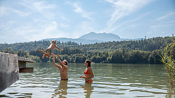 Eltern planschen mit ihrem Kind im See beim Familienurlaub in Tirol.
