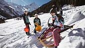 Kinder rutschen die Piste mit Rodeln hinunter nahe des Familienhotels Bella Vista in Südtirol.