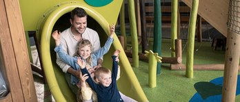 Vater mit seinen beiden Töchtern auf der Rutsche auf dem Indoor-Spielplatz im Familienhotel
