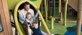 Vater mit seinen beiden Töchtern auf der Rutsche auf dem Indoor-Spielplatz im Familienhotel