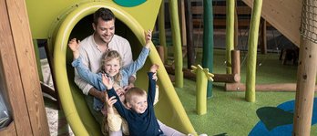 Vater mit seinen beiden Töchtern auf der Rutsche auf dem Indoor-Spielplatz im Familienhotel