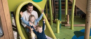 Vater mit seinen beiden Töchtern auf der Rutsche auf dem Indoor-Spielplatz im Familienhotel