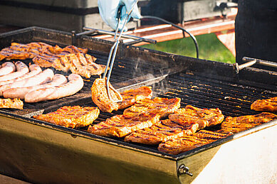 Auf einem großen Grill werden Fleisch und Wurstwaren frisch gegrillt. 