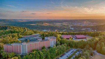 Luftaufnahme des Familienhotels Sonnenhügel bei Sonnenuntergang, eingebettet in die idyllische Landschaft des Bayerischen Waldes mit umgebenden Wäldern und sanften Hügeln.