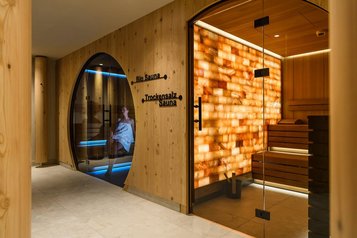 Saunabereich im Zauchenseehof mit moderner Bio-Sauna, beleuchteter Trockensalz-Sauna und einer Person, die entspannt in der blau beleuchteten Kabine sitzt.