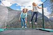 Zwei Mädchen springen auf dem Trampolin draußen auf dem Außengelände des Kinderhotels Sailer in Tirol.