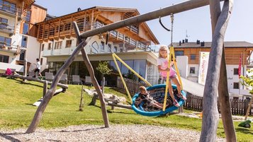 Großer Outdoor-Spielplatz, wo Kinder in der Nestschaukel sitzen im Familienhotel Almfamilyhotel Scherer in Tirol.