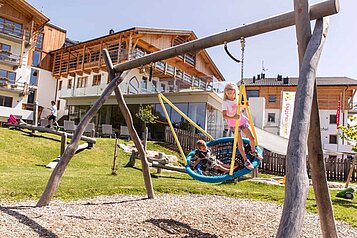 Großer Outdoor-Spielplatz, wo Kinder in der Nestschaukel sitzen im Familienhotel Almfamilyhotel Scherer in Tirol.