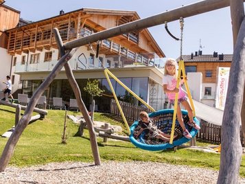 Großer Outdoor-Spielplatz, wo Kinder in der Nestschaukel sitzen im Familienhotel Almfamilyhotel Scherer in Tirol.