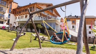 Großer Outdoor-Spielplatz, wo Kinder in der Nestschaukel sitzen im Familienhotel Almfamilyhotel Scherer in Tirol.