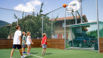 Kinder spielen Basketball auf dem umzäunten Fun-Court des Familienhotels Krone im Allgäu.