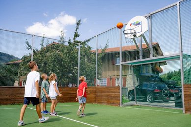 Kinder spielen Basketball auf dem umzäunten Fun-Court des Familienhotels Krone im Allgäu.