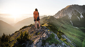 Wandern in Liechtenstein: Frau wandert auf dem Fürstin Gina Weg. Die Abendsonne verschwindet hinter den Bergen.