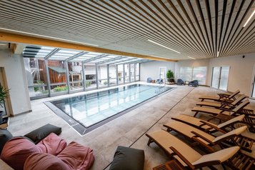 Moderner Indoor-Pool mit großen Glasfronten und Relaxliegen im Familienhotel Bruckwirt.