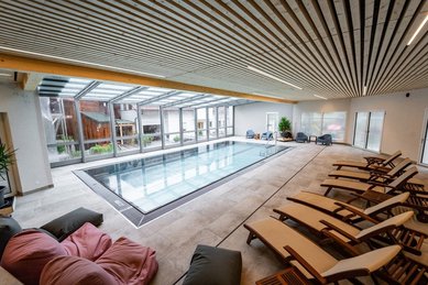 Moderner Indoor-Pool mit großen Glasfronten und Relaxliegen im Familienhotel Bruckwirt.