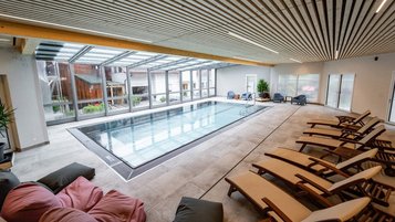 Moderner Indoor-Pool mit großen Glasfronten und Relaxliegen im Familienhotel Bruckwirt.