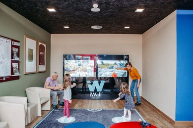 Familie mit zwei Kindern spielt an einer interaktiven iWall-Spielewand im AIGO Welcome Family Bereich.