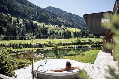 Eine Dame sitzt im Freiem im Whirlpool und genießt die Aussicht auf die Landschaft im Familienhotel Alphotel Tyrol Wellness & Family Resort in Südtirol.