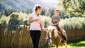 Im Familienhotel Alpura Retreat in Südtirol reitet ein Kind fröhlich auf einem Pony durch die Natur.