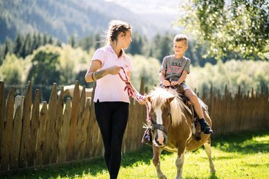 Im Familienhotel Alpura Retreat in Südtirol reitet ein Kind fröhlich auf einem Pony durch die Natur.