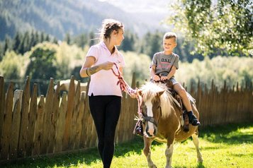 Im Familienhotel Alpura Retreat in Südtirol reitet ein Kind fröhlich auf einem Pony durch die Natur.