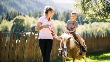 Im Familienhotel Alpura Retreat in Südtirol reitet ein Kind fröhlich auf einem Pony durch die Natur.