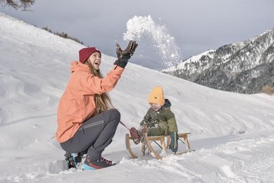 Kind und Mutter spielen im Schnee beim Winterurlaub am Familienhotel Gorfion in Liechtenstein.