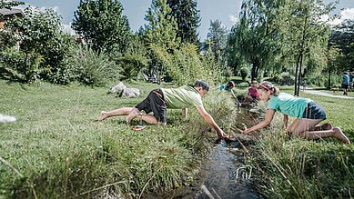 Im Familienhotel Alpenhof Dolomit Family in Südtirol spielen Kinder draußen am Wasser.